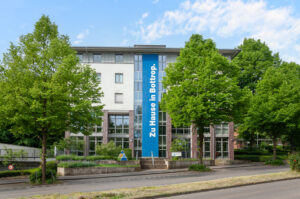 Das GBB-Bottrop Unternehmensgebäude zeigt ein großes Banner mit der Aufschrift 'Zu Hause in Bottrop'. Umgeben von grünen Bäumen und einer modernen Architektur vermittelt es eine einladende Atmosphäre.